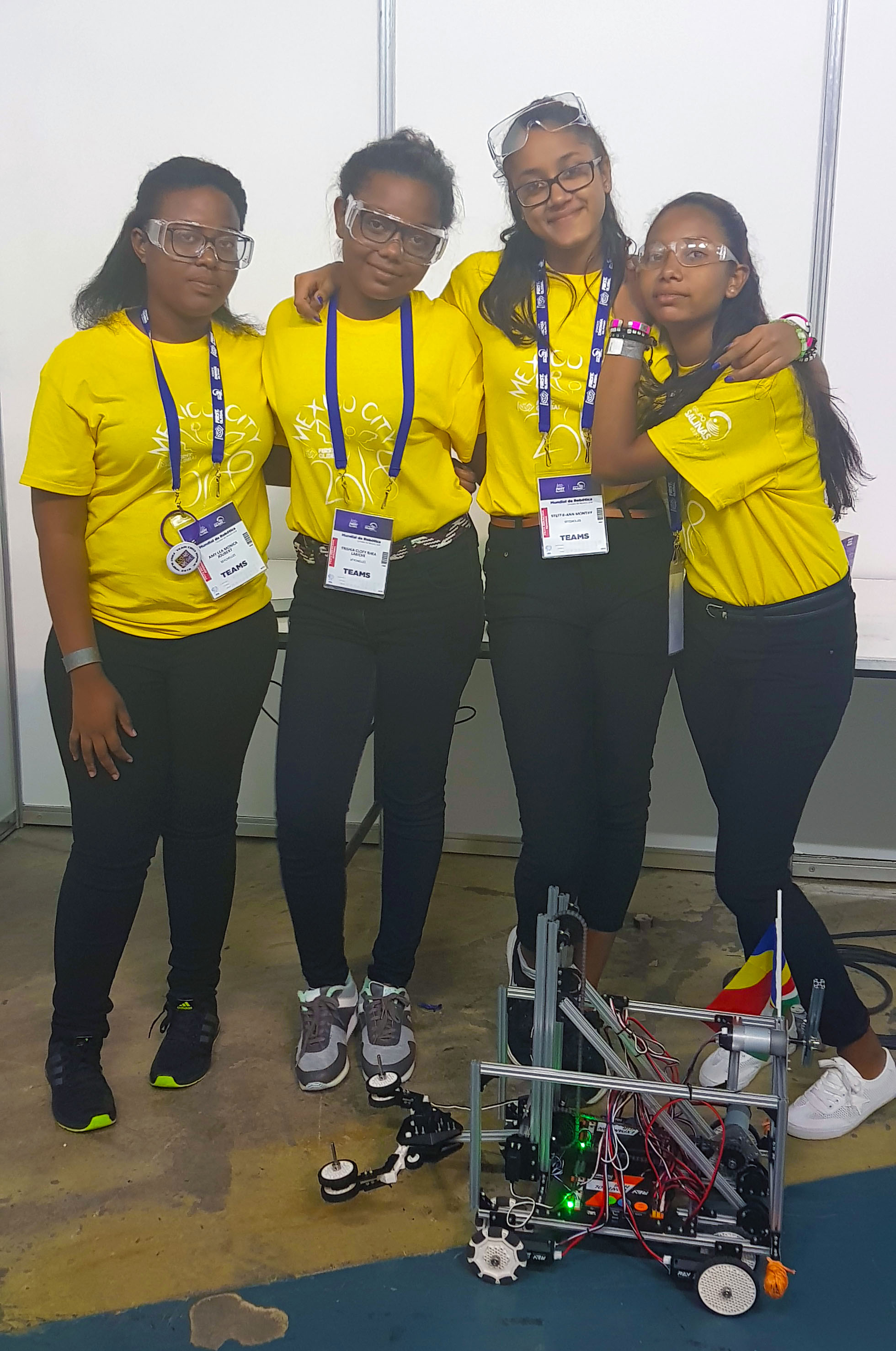 four girls in yellow shirts standing with a robot 