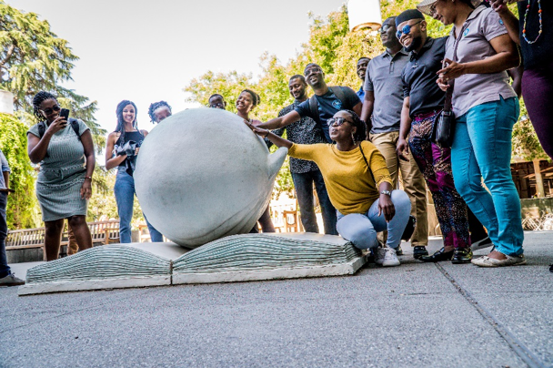 a group of adults rubbing a statue of a head in a book 