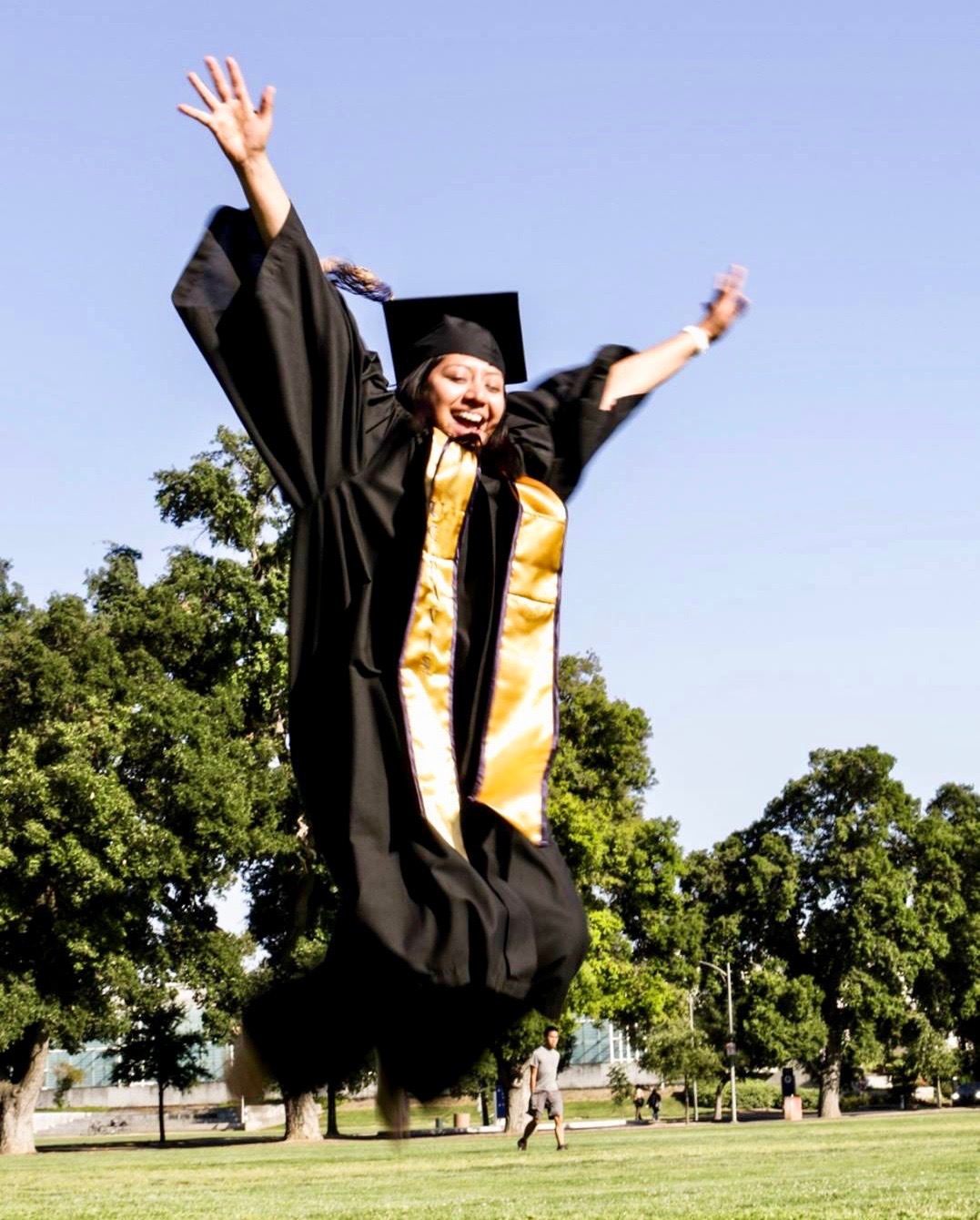 Itzel Morales jumping in air in graduation attire
