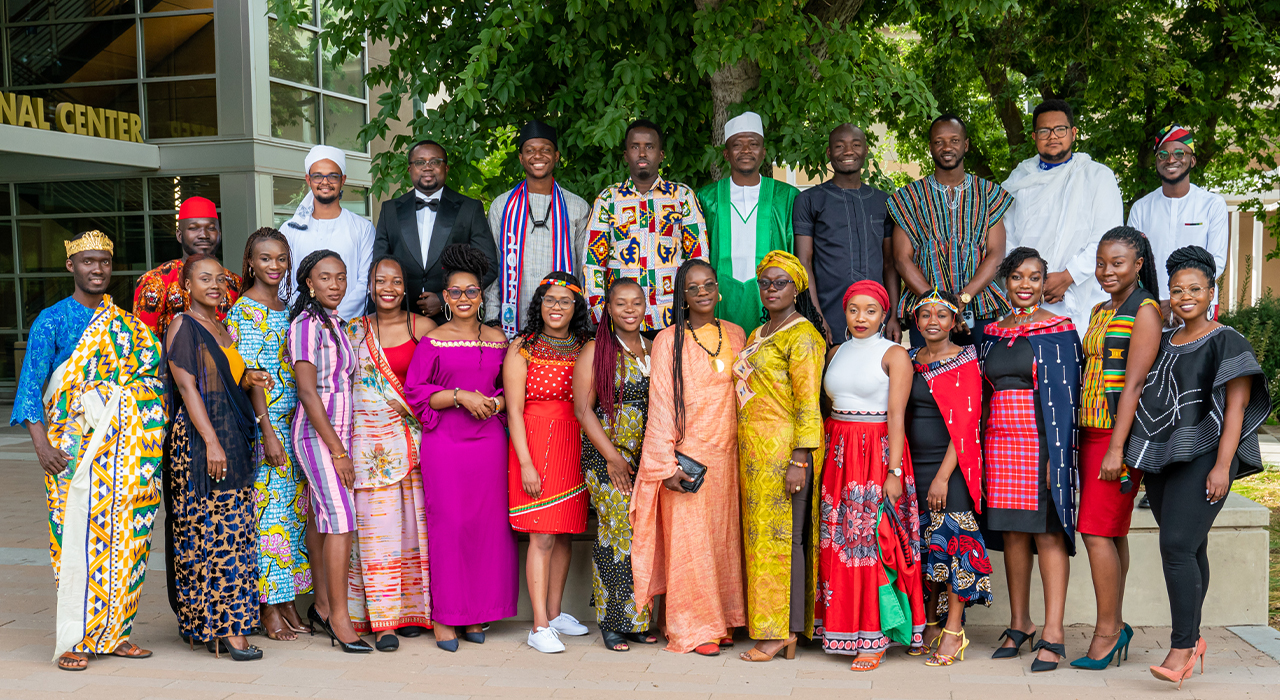 25 Fellows in the 2022 UC Davis Mandela Washington Fellowship pose under a large tree wearing traditional cultural dress and business wear.