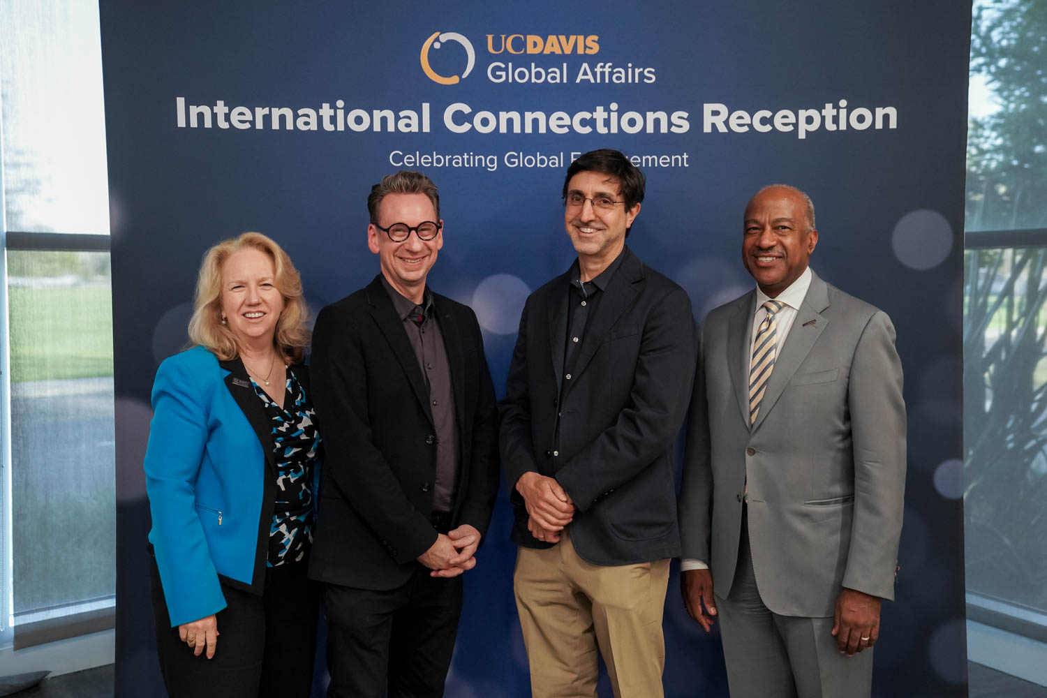 Four people stand in front of a backdrop and smile at the camera