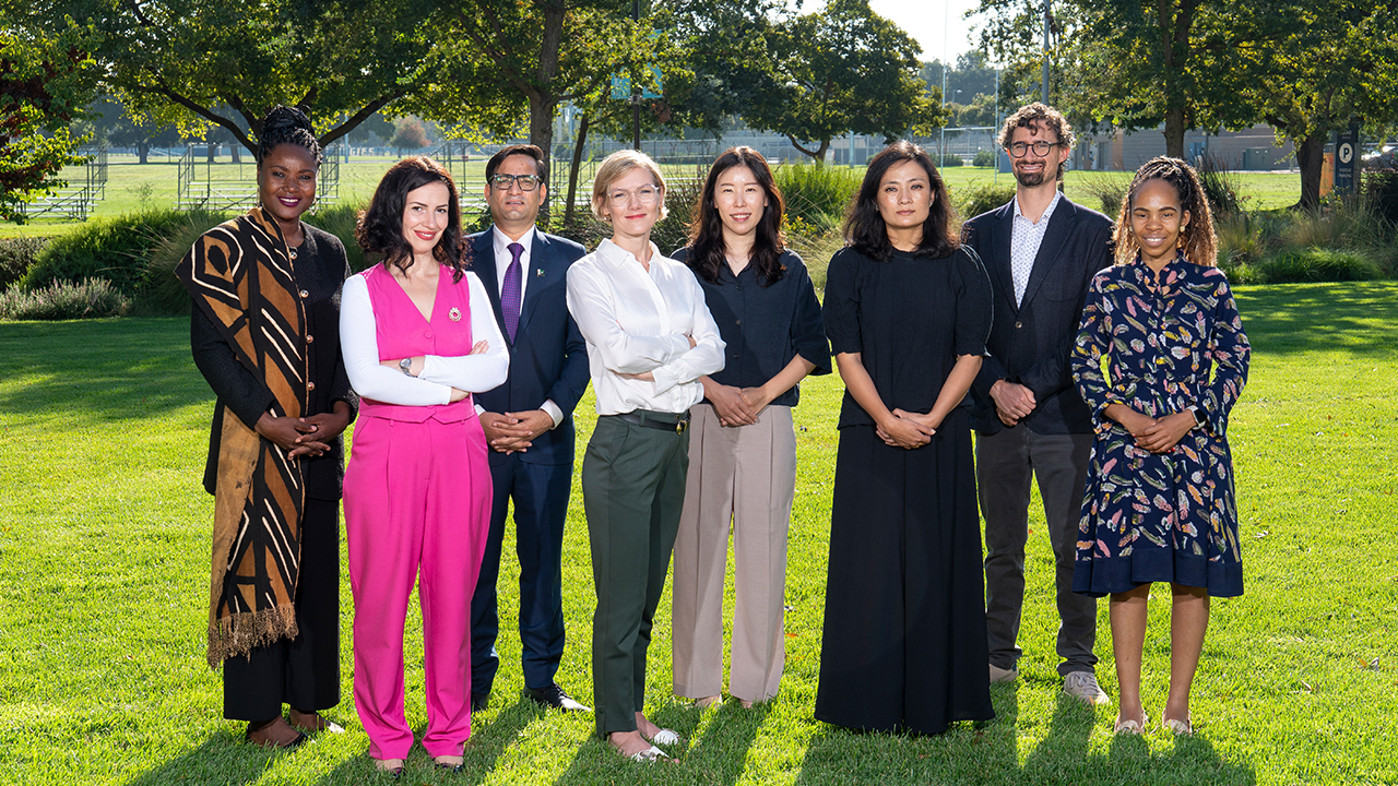 A group photo of eight Humphrey Fellows dressed in business attire stand on the grass with trees in the background.