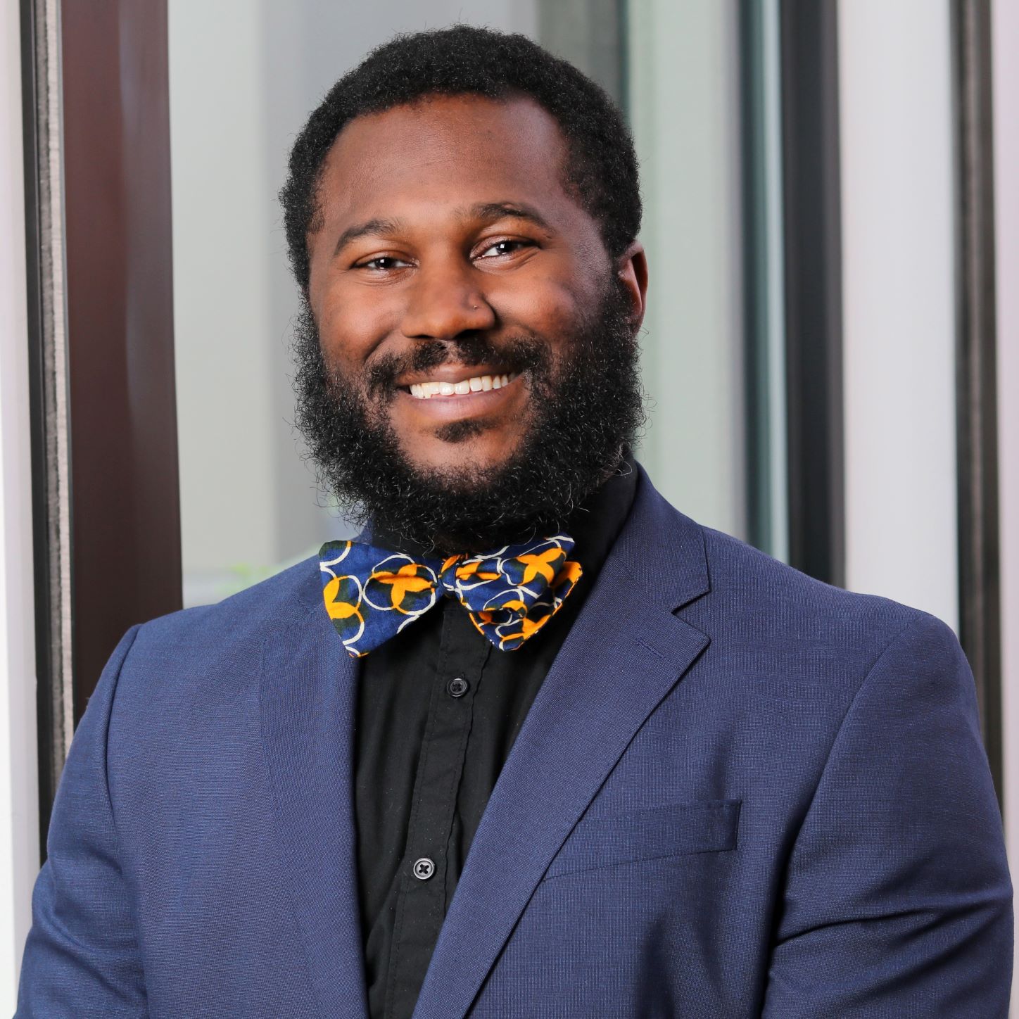 A.P. Moore smiles at the camera while wearing a navy blue suit and multicolored bow tie with a black collared shirt. 
