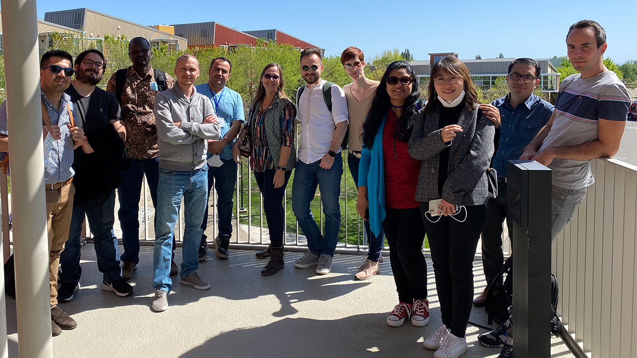 Twelve Humphrey fellows stand outside in the sunlight on a balcony overlooking part of the UC Davis campus