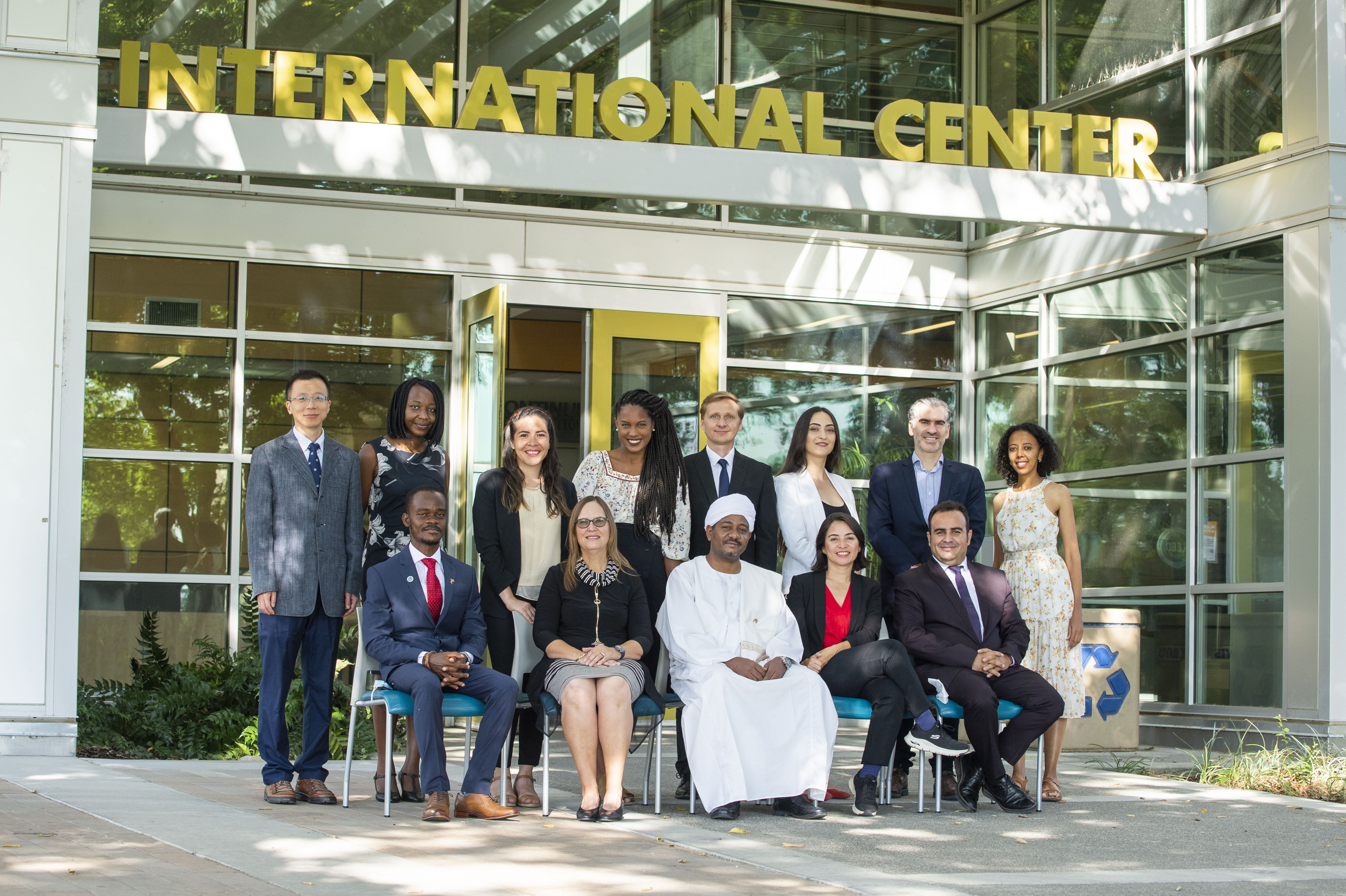 Eight Humphrey fellows stand in front of the entrance of the International Center on the UC Davis campus. Seated in front of them are four other Humphrey fellows and Karen Beardsley of Global Affairs. 