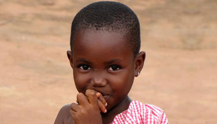 A child stares into the camera with her hands in her mouth.