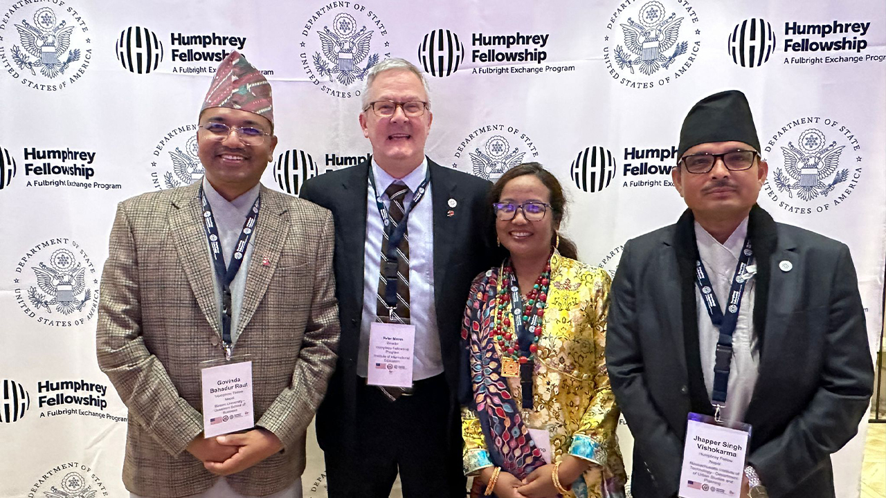 Sushila stands with three other men, two from her home country and one American from IIE in front of a white backdrop with the Department of State and Humphrey Fellowship logos in navy blue. 