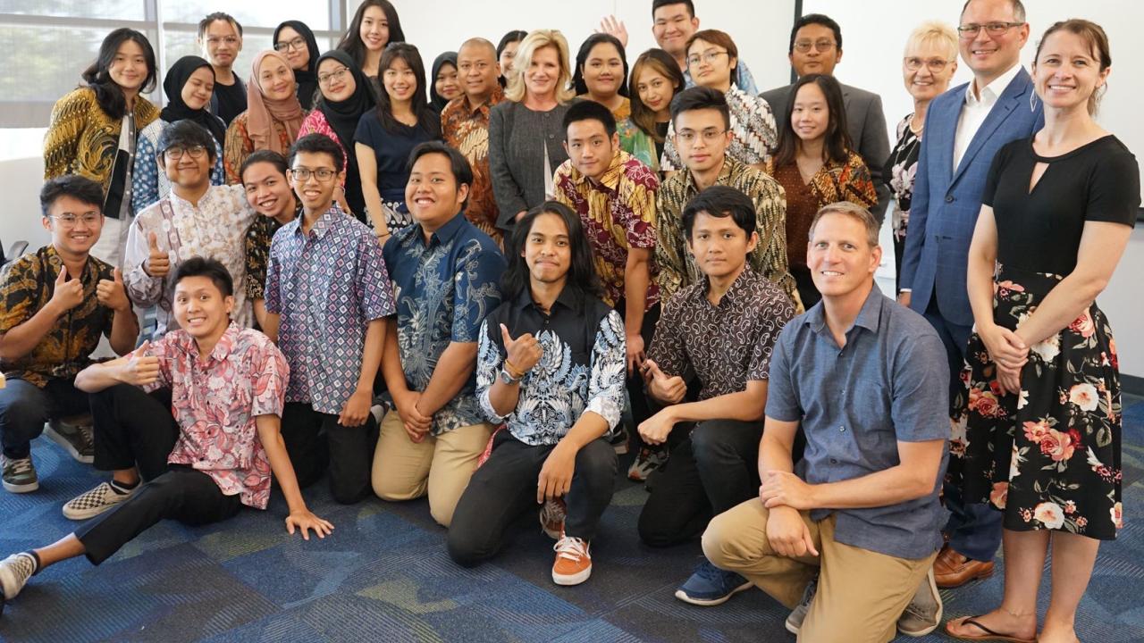 32 people, many of whom are male and female students visiting from Indonesia, pose in rows with some students giving thumbs up.