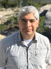 Samuel Sandoval Solis smiles looking at the camera while wearing an off white collared short sleeve shirt. 