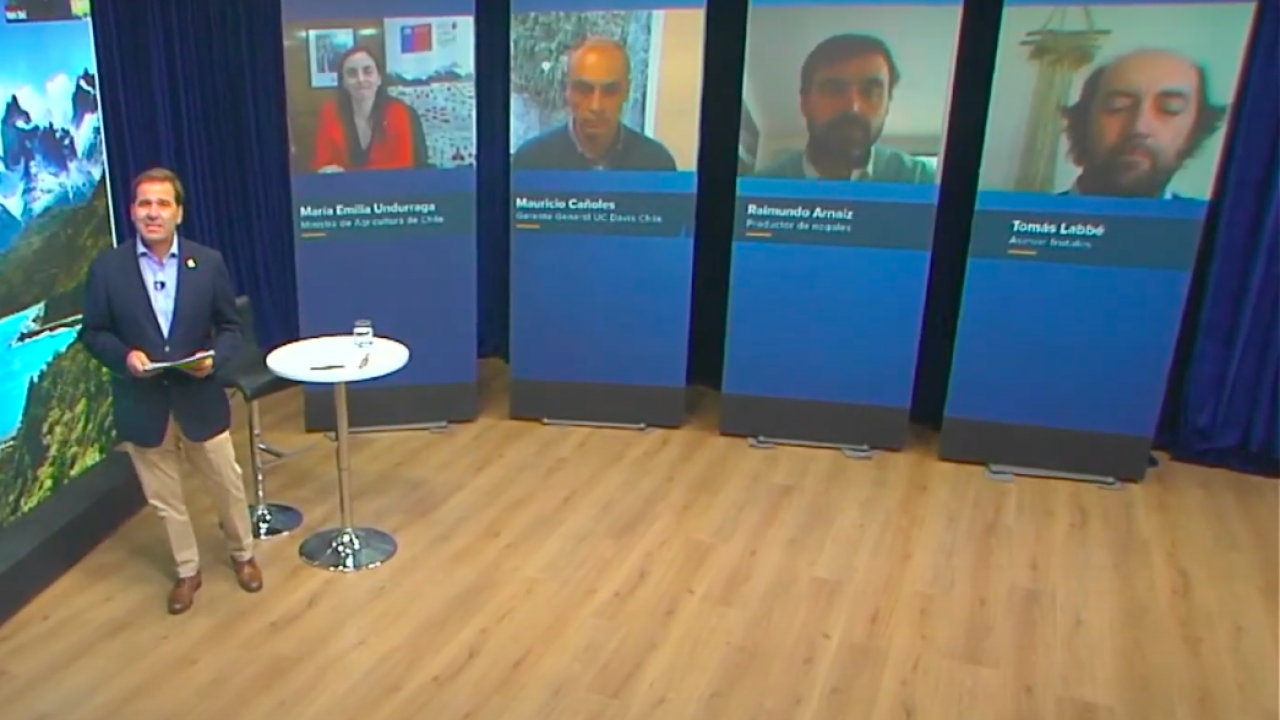 Photo of a man in a suit standing next to digital screen with other presenters.