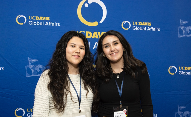 Two women smiling in front of a blue UC Davis Global Affairs logo backdrop