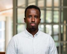 Mohamed wears a light blue and white striped collared shirt. 