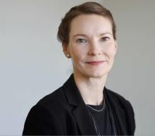 Professional woman with a warm smile, wearing a black blazer, against a neutral background.
