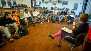 A group of students sit in a semi circle looking at the vice provost and dean at th