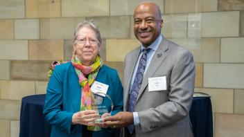 Beth Greenwood and Chancellor Gary May smile at the camera while holding an award