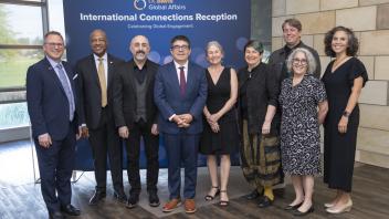 Ten UC Davis faculty and staff members in formal attire in front of an International Connections Reception backdrop