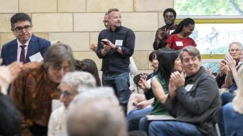 People seated and standing in a room, some clapping and listening attentively
