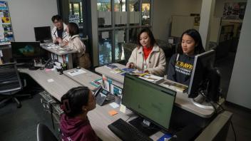 Two students stop by a welcome desk to chat with another student