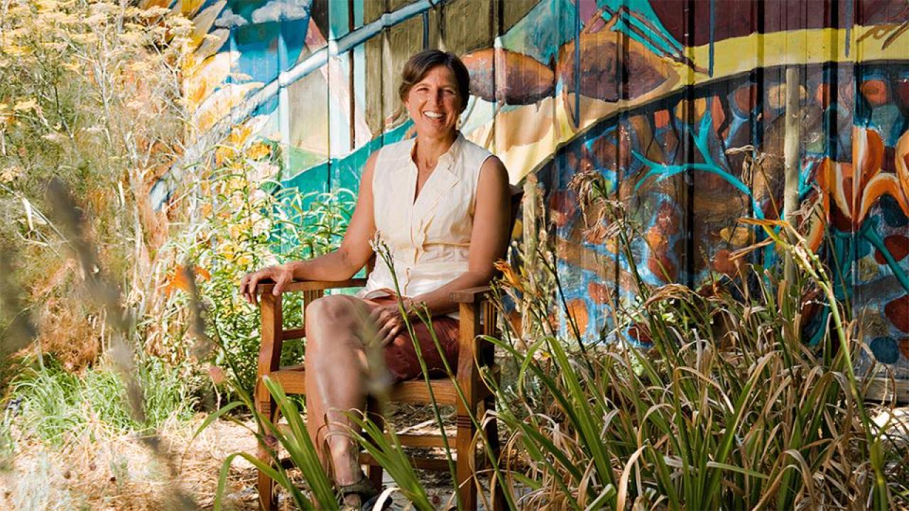 Pamela Ronald sitting on chair next to plants and art. 