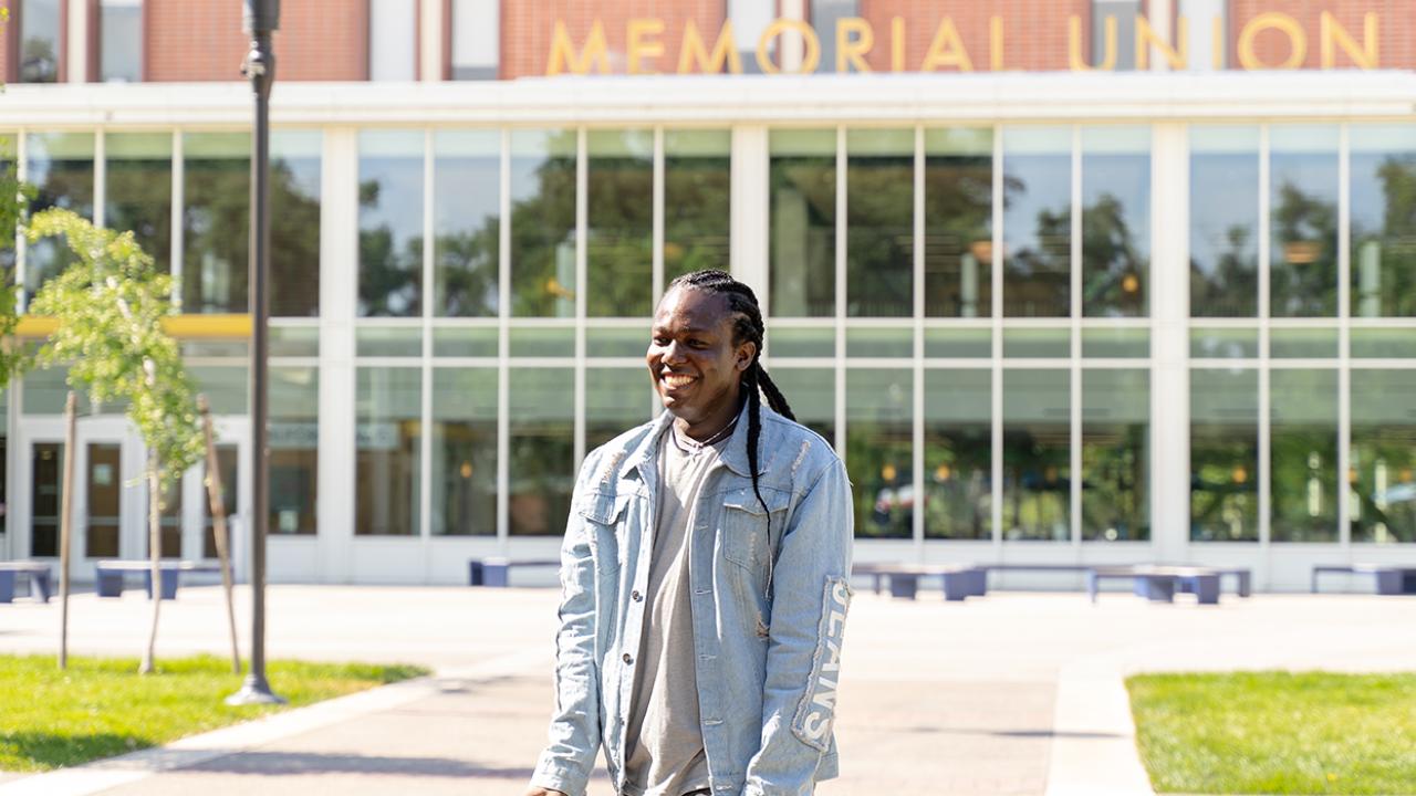 Kelsey Kalu looks at someone off to the left and smiles at them. Behind Kelsey is the Memorial Union building on the UC Davis campus, with a gold lettering that reads "Memorial Union."