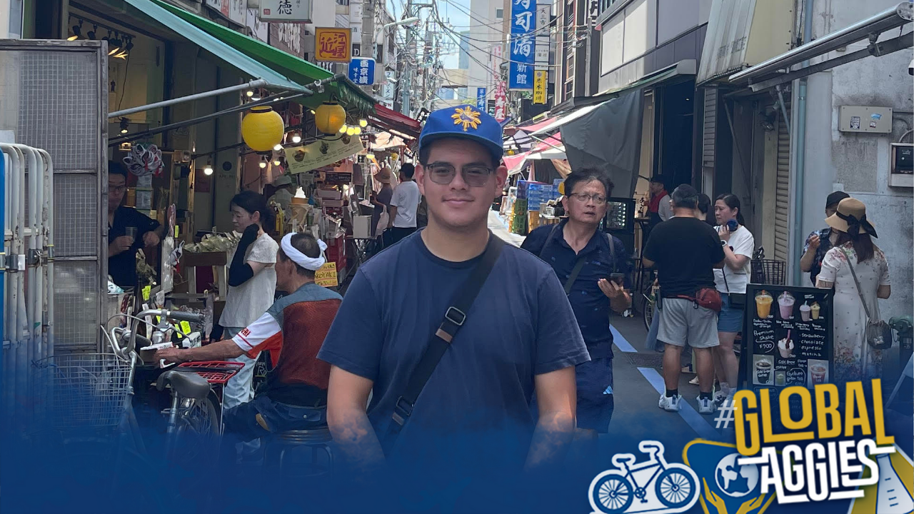 Aidan stands on a crowded street with the Global Aggies logo in the bottom right-hand corner.