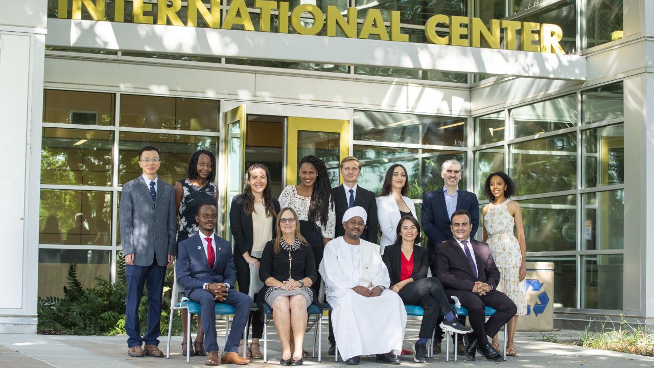 Eight Humphrey fellows stand in front of the entrance of the International Center on the UC Davis campus. Seated in front of them are four other Humphrey fellows and Karen Beardsley of Global Affairs.