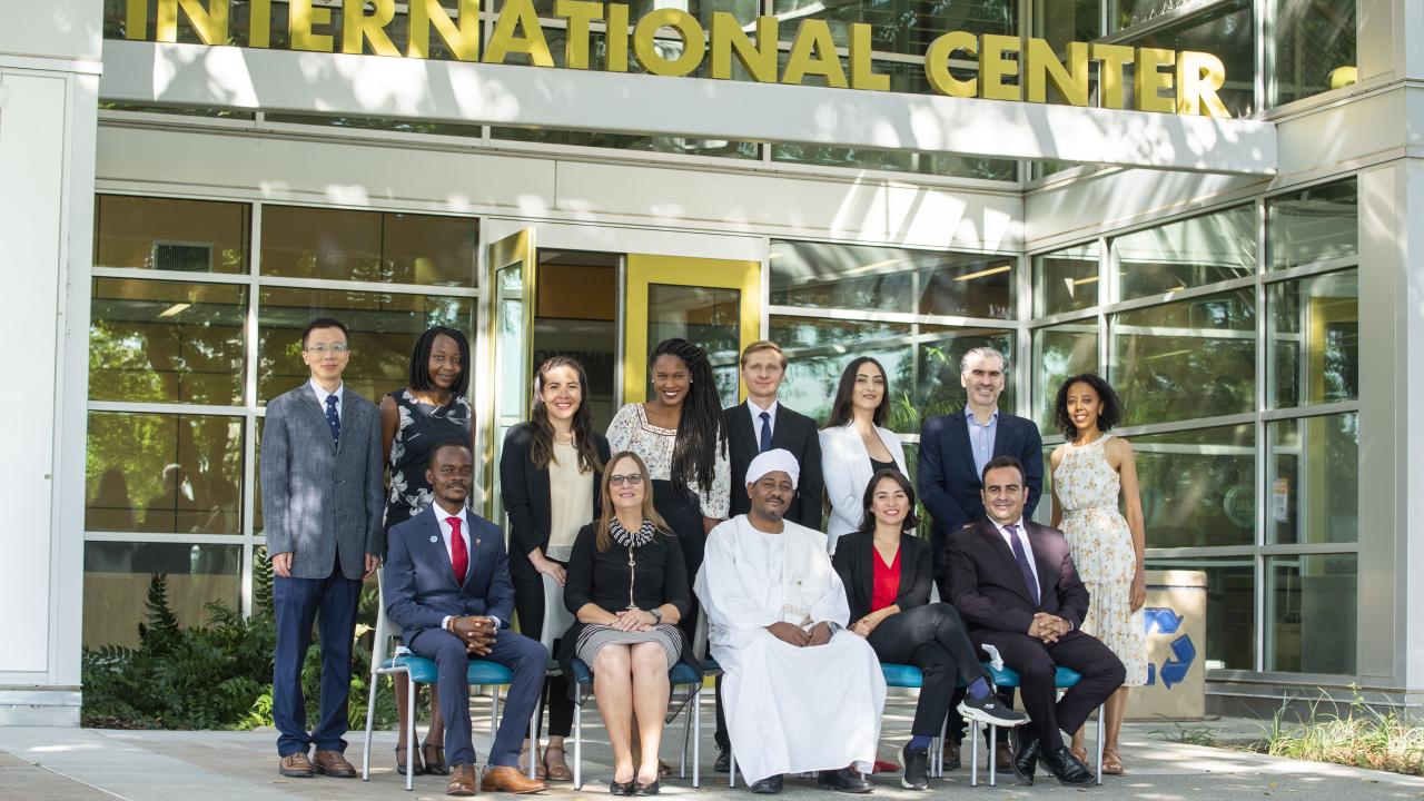 Eight Humphrey fellows stand in front of the entrance of the International Center on the UC Davis campus. Seated in front of them are four other Humphrey fellows and Karen Beardsley of Global Affairs. 