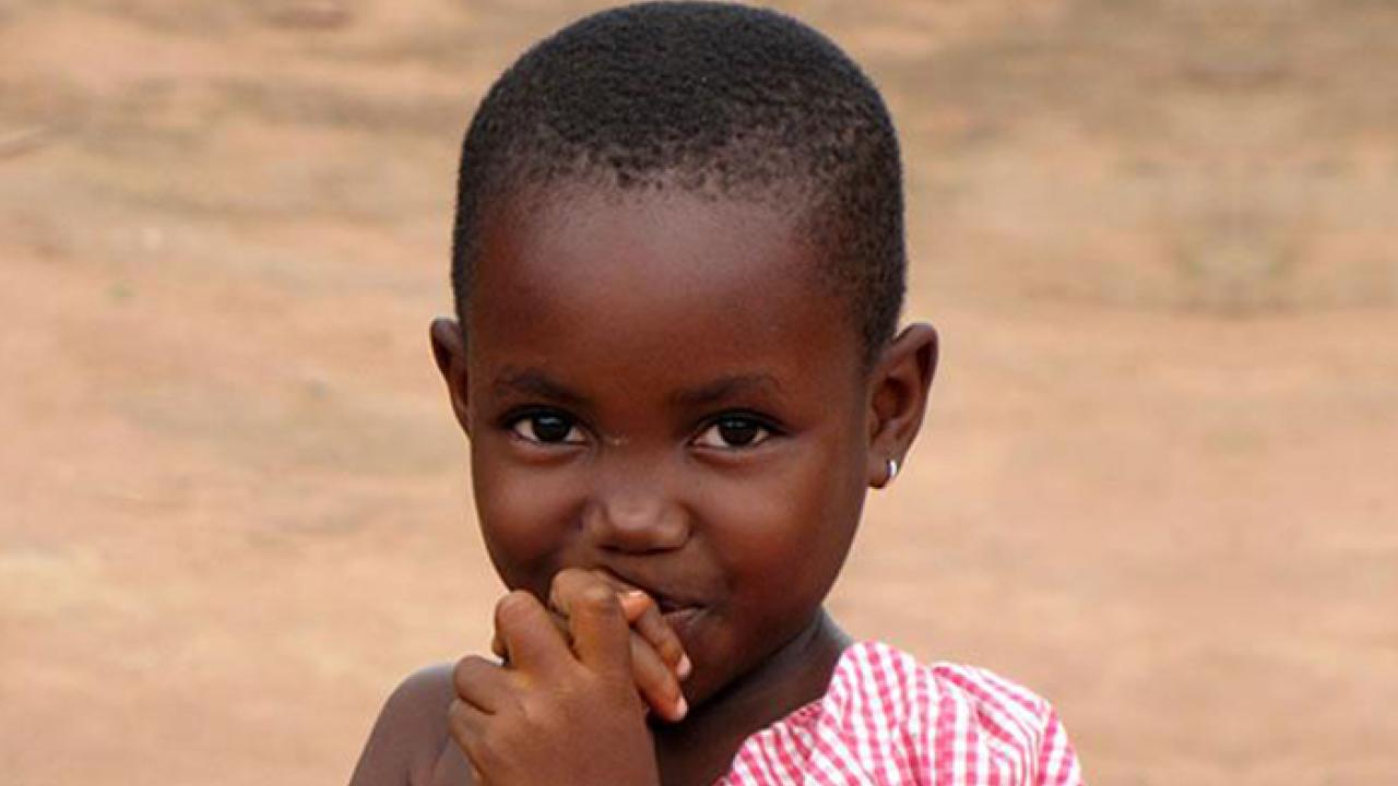 A child stares into the camera with her hands in her mouth.