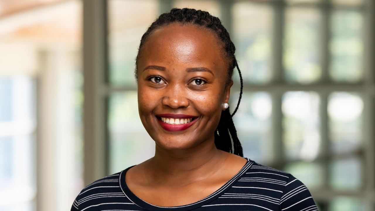Gloria wears a black, gray and white striped top while she smiles at the camera