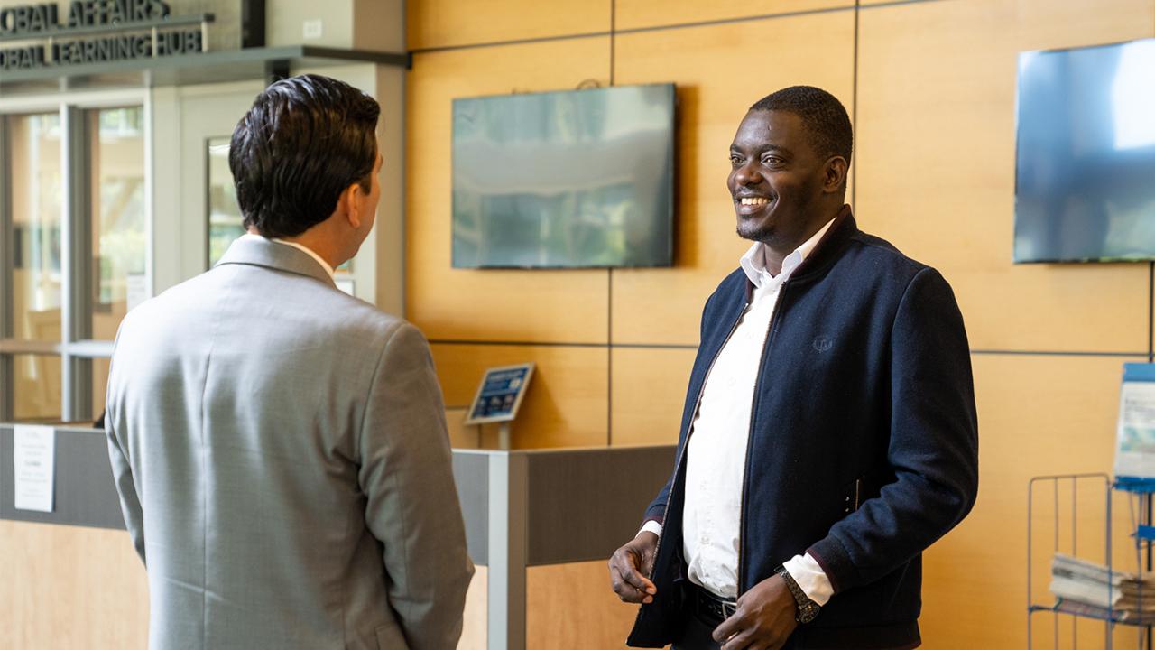 Silas stands in the lobby of the International Center and smiles as he speaks to a colleague standing in front of him.