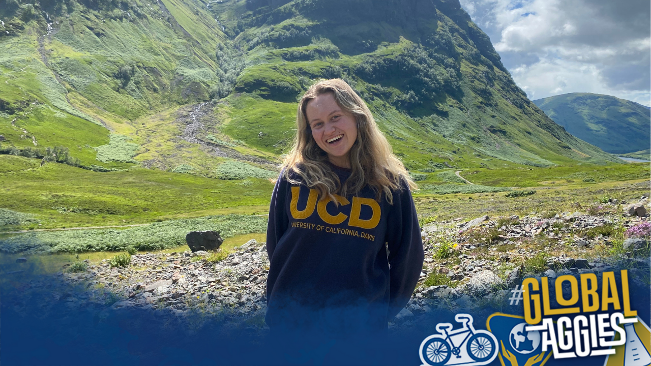 UC Davis student Anya Nygaard smiles at the camera wearing a UCD sweatshirt with the Scottish Highlands in the background. A blue watercolor overlay with Global Aggies is over the bottom of the photo.