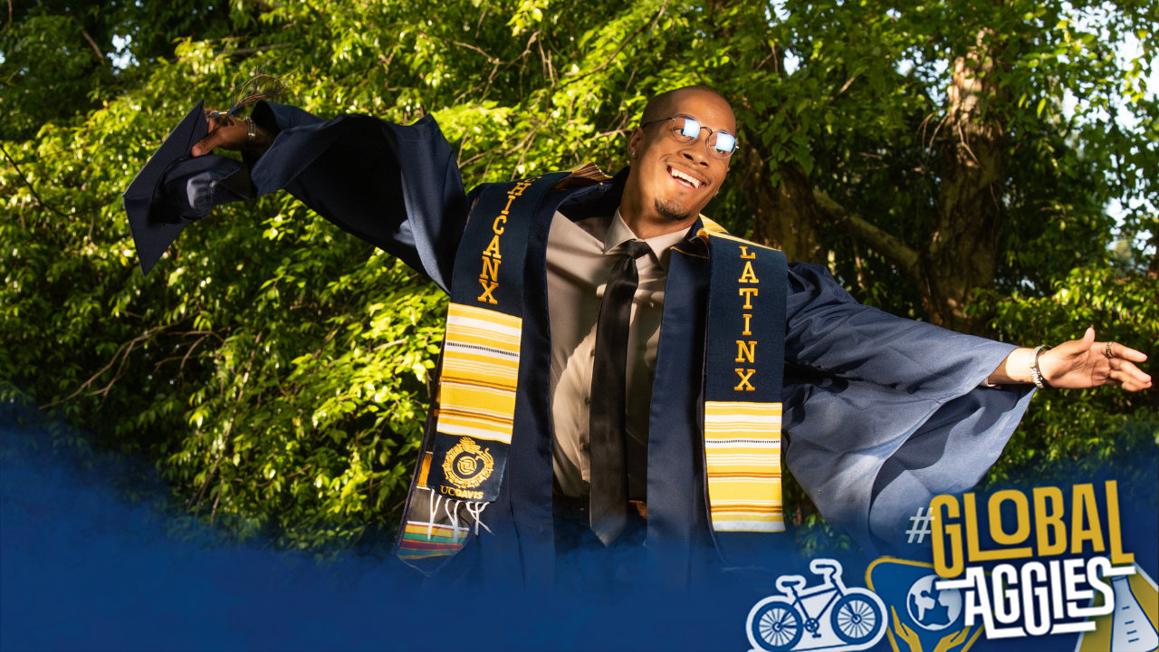 Mahiri Comeaux leaps in the air with arms outstretched wearing a commencement robe and Chicanx/Latinx stole