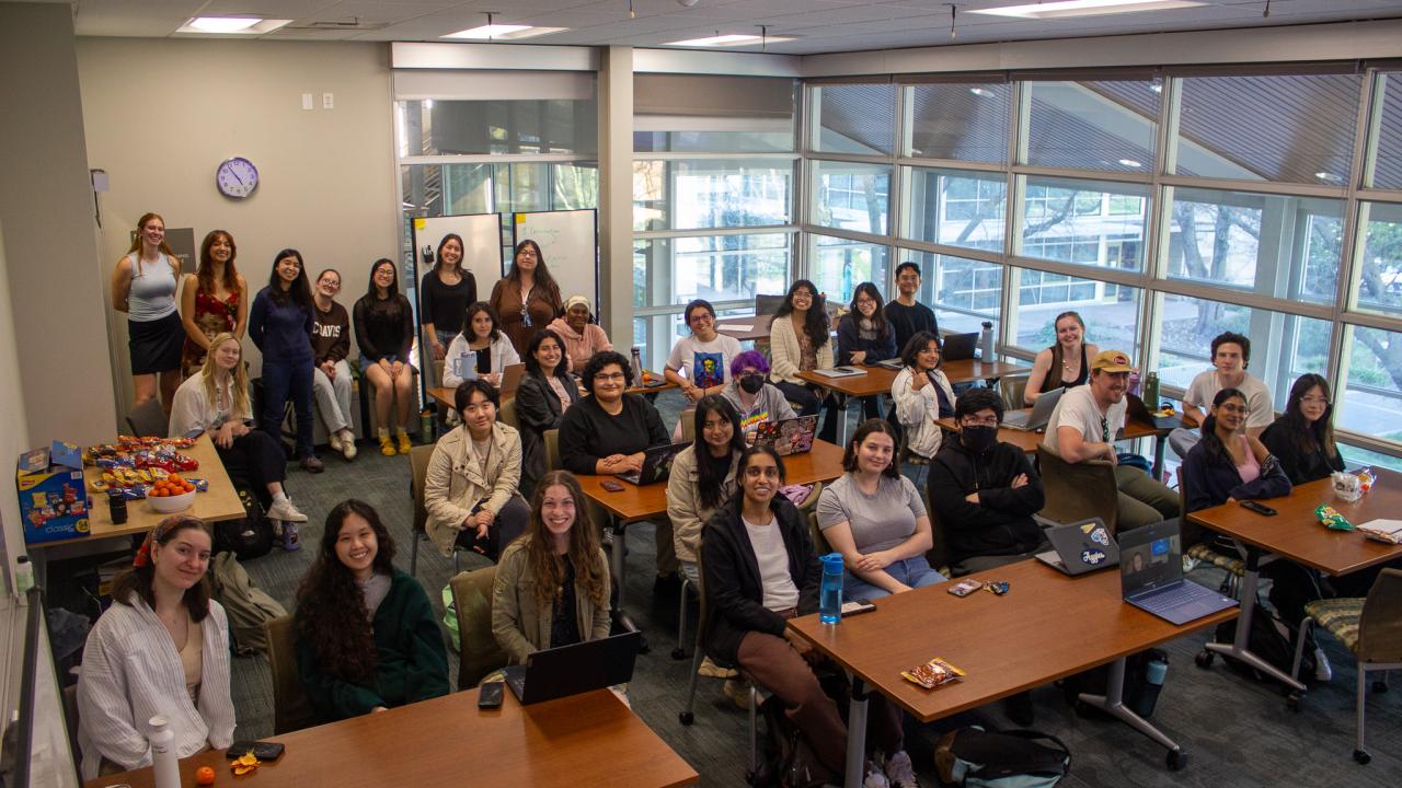 Students sit around their desk smiling for the camera.