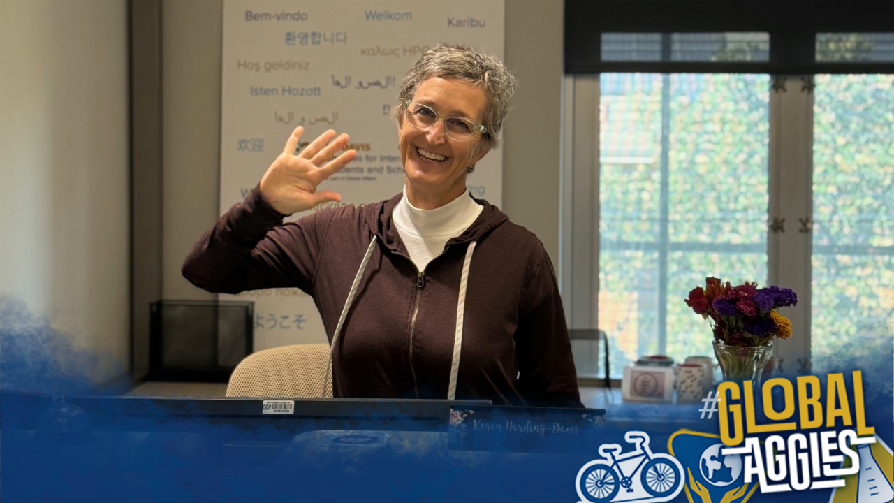 Karen Harding smiles and waves at the camera from behind the welcome desk