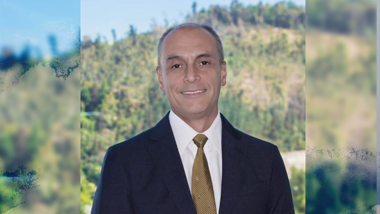 Photo of Mauricio Cañoles in a dark suit and a gold tie smiling at the camera