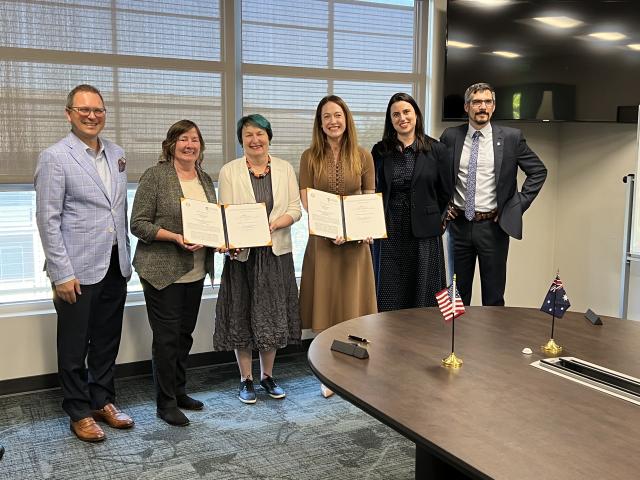 Joanna Regulska, Michael Lazzara, and the Provost gather around a document to sign an international agreement.