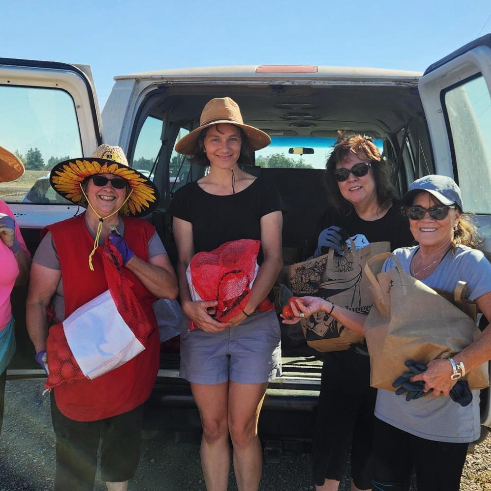 Five people pose with bags of produce in front of a white van in a rural setting.