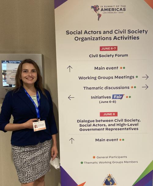 Paulina Carmona-Mora in front of standing banner with agenda for social actors and civil society organizations activities