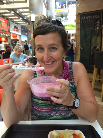 Karen sitting and eating a pink soup with people and posters in the background.