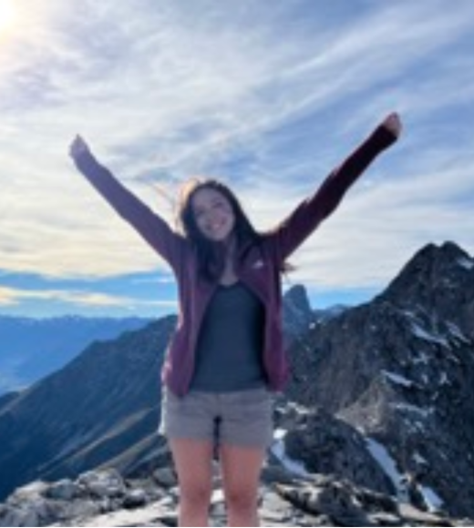 Stella Baum raising her arms with a scenic background behind her.