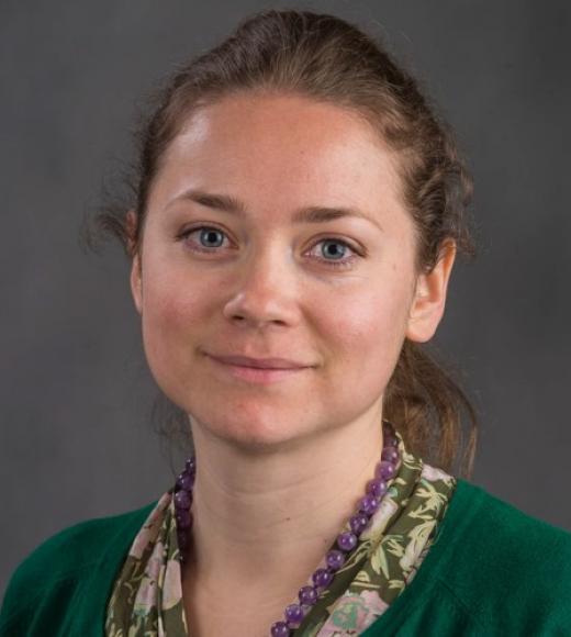 Lena smiles in a green shirt with a gray background.