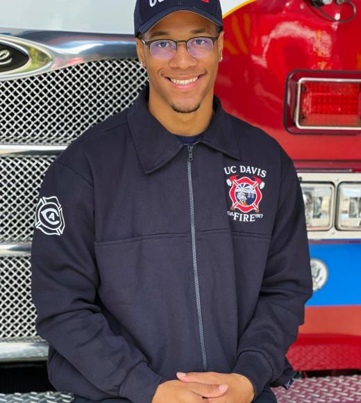 Comeaux seated on a fire truck with a blue UC Davis fire department jacket and hat.