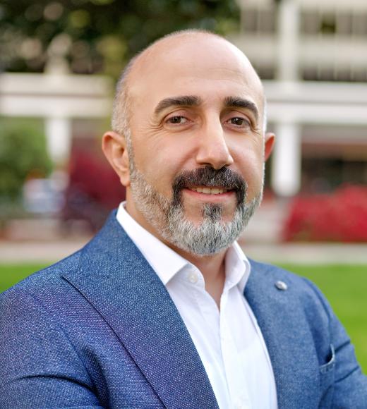 Man with a beard in a blue blazer, smiling outdoors