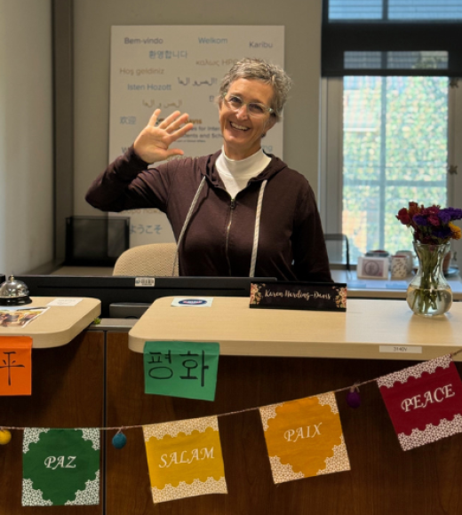Karen Harding waving at camera from behind a desk. 