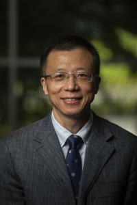 Huiyong Zhang smiles in a 2021 headshot. His black hair is short and neatly styled. He wears rectangular framed glasses, a gray blazer, white collared shirt, and a navy blue tie with small white fishes. 