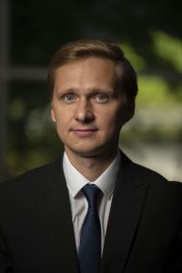 Sergey Vassilyev posed for a headshot in 2021. He has short blonde hair that is neatly styled. He wears a black blazer, white collared shirt, and navy blue tie.