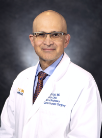 Dr. Bob Kiaii sits in front of a dark gray background. He wears a white medical jacket over a blue collared shirt and a dark tie with a circular pattern. The jacket is embroidered with "B Kiaii, MD, Division Chief, Medical Professor, Cardiothoracic Surgery."