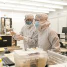 Two scientists in full cleanroom suits pointing at a computer monitor in a sterile lab.
