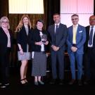 Six professionals stand on a stage, smiling. The woman in the center holds an award.