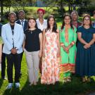 The 12 Humphrey Fellows stand posed in two rows outside on grass with an open lawn and bushes in the background.